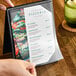 A hand holding a clear vinyl sheet protector with a menu inside.