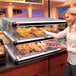 A woman taking food from a Hatco countertop display case.