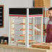 A tall, glass display cabinet with four circular racks holding pizzas, designed for keeping food warm and visible in a restaurant setting.