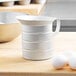 A white Vollrath aluminum measuring cup on a wooden table next to eggs.