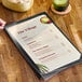 A hand holding a menu on a table with a clear vinyl sheet protector over it.
