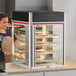 A woman in a bakery kitchen wearing an apron using a Hatco Flav-R-Savor countertop display case.