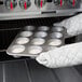 A person in gloves holding a Chicago Metallic Jumbo Pecan Roll / Muffin Pan filled with muffins.