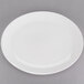 A Tuxton Modena AlumaTux Pearl White oval china platter with a rim on a gray surface.