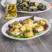 A Tuxton Modena AlumaTux Pearl White china platter with mussels and a lemon wedge on a table.