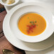 A close-up of a Tuxton AlumaTux Pearl White plate with a bowl of soup on it.