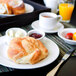 A Tuxton AlumaTux Pearl White china plate with a knife and a croissant on a table with a cup of coffee and a bowl of butter.