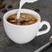 A Tuxton white espresso cup with brown and white liquid in it and milk being poured into it.