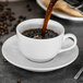A cup of coffee being poured into a white saucer.