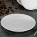 A Tuxton Modena AlumaTux Pearl White china saucer on a table.