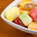 A Tuxton bright white square china bowl filled with fruit including grapes, pineapple, and melon.