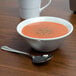 A Tuxton TuxTrendz bright white china bowl filled with soup on a table with a spoon.
