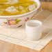 A white porcelain cup filled with liquid next to a bowl of soup.