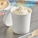 A Choice white paper food cup filled with ice cream on a counter with a wooden spoon.