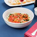 A Tuxton porcelain bowl filled with pasta and sauce with a glass of wine on a table.