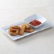 A Tuxton white rectangular china tray with fried onion rings and red sauce.