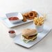 A Tuxton rectangular white china tray with a hamburger and fries and a cup of ketchup.