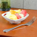 A Tuxton bright white square china bowl filled with fruit on a table with a fork.