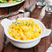 A bowl of macaroni and cheese in a Tuxton bright white china casserole with two lug handles on a table.