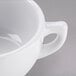 A close-up of a Tuxton TuxTrendz bright white cappuccino cup with a handle.