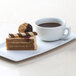 A white plate with a piece of cake and a Tuxton bright white cappuccino cup on a table.