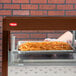 A person holding a tray of french fries in front of a Hatco countertop hot food display warmer.