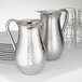 An American Metalcraft mirror finish stainless steel bell pitcher next to plates.