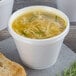 A white foam food container filled with soup with noodles and green onions.