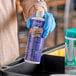 A person in blue gloves holding a bottle of Noble Chemical QuikSan Nickel-Safe ice machine sanitizer.