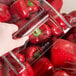 A hand holding a Cambro clear plastic container of red peppers.