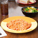 A bowl of salad with colorful vegetables in a yellow melamine bowl on a table with a plate of spaghetti.