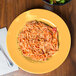 A plate of spaghetti with sauce, a bowl of salad, and a yellow melamine bowl on a table.