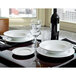 A white Tuxton china bowl on a table with plates and a wine glass.