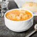 A Tuxton AlumaTux Pearl White China stackable soup cup filled with soup next to bread and a spoon.