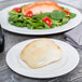 A Tuxton AlumaTux Pearl White china plate with a bread roll and salad on it.