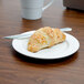 A Tuxton AlumaTux Pearl White China plate with a croissant and a cup of coffee on it.