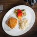 A Tuxton oval china platter with rice, vegetables, and chicken on it.