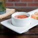 A white Tuxton AlumaTux ramekin filled with sauce on a plate of food with shrimp and vegetables.