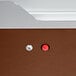 A brown surface with a red button in a hole and a round button.