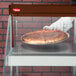 A person wearing a white glove using a Hatco countertop glass display case to serve a pizza.