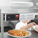 A Hatco dual infrared warmer above plates of hot dogs, fries, and a sandwich on a counter.