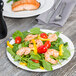 A Tuxton AlumaTux Pearl White china plate with a shrimp and spinach salad with tomatoes and peppers on a table.