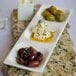 A Tuxton rectangular china plate with green olives, feta cheese, and a glass of wine.