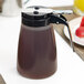 A brown Tablecraft polypropylene dispenser with a black lid.