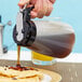 A person using a Tablecraft black polypropylene dispenser to pour syrup on pancakes on a plate.