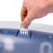 A hand using a San Jamar Arctic Blue Ultrafold Fusion towel dispenser to put a white object in a plastic container.