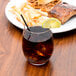 A Chef & Sommelier double old fashioned glass of brown liquid with a lemon wedge on top of a plate of food.