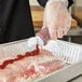 A hand using a Chef Master squeeze bottle to pour sauce on meat.