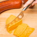 A hand using a Franmara stainless steel cheese knife to cut cheese on a counter.