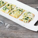 A rectangular white porcelain platter with cheese, bread, and vegetables on it.